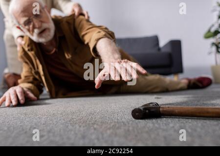 fuoco selettivo dell'uomo anziano caduto che prova ad ottenere bastone camminante mentre moglie lo aiuta Foto Stock