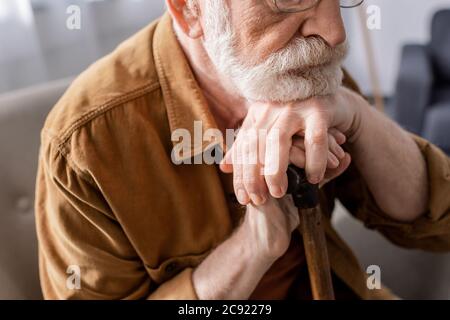 vista tagliata dell'uomo anziano depresso seduto e appoggiato sul bastone da passeggio Foto Stock