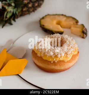 Primo piano di una ciambella con crema gialla e cocco fiocchi su un piatto con fette di ananas Foto Stock