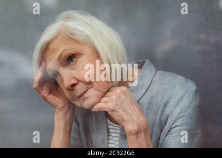 solitaria donna anziana che si allontana mentre si alza dalla finestra Foto Stock