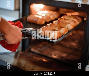 Colpo di closeup di un panettiere che rimuove i panini appena fatti da un forno utilizzando pinze metalliche Foto Stock