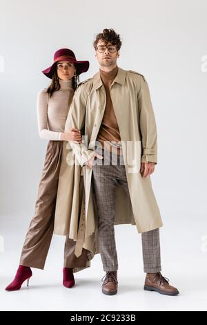 vista completa di una donna elegante in cappello che tocca la mano di un uomo alla moda in trench cappotto grigio Foto Stock