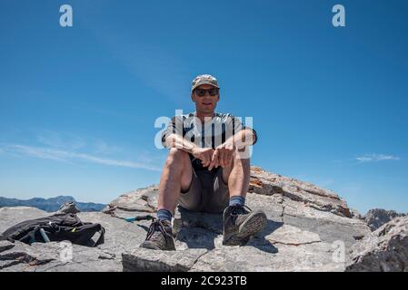 Un uomo di mezza età si siede sulla cima rocciosa della montagna Foto Stock