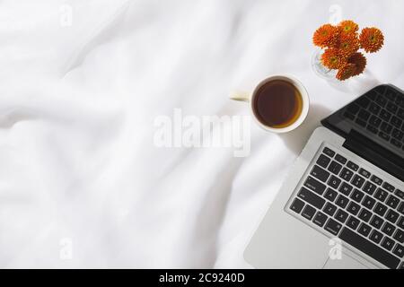 Vista dall'alto del tè del mattino in tessuto voile con un computer portatile, tazza di tè e un vaso di fiori arancioni con spazio per il testo Foto Stock