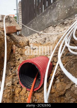 I cavi fuoriescono dal tubo di sicurezza scanalato in strada, dettaglio di uno scavo. Internet e società di fornitori di dati che costruiscono il conne pshychical Foto Stock