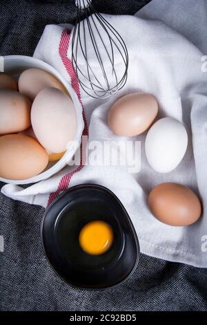 Immagine di tuorlo d'uovo in una ciotola accanto a uova sane in un piatto o un panno bianco e utensili da cucina. Foto Stock