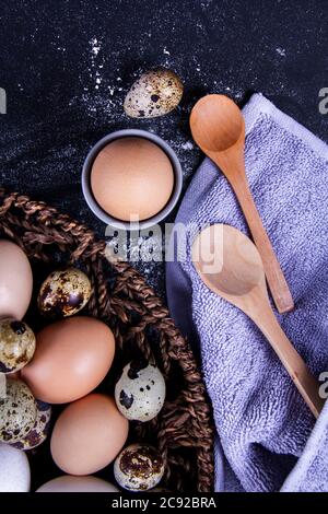 Alcune uova e uova di quaglia sane sono in un cestino di legno vicino ad un cucchiaio di legno. Foto Stock