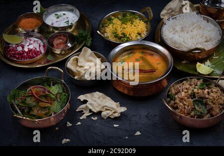 Piatti vegetariani dell'India del Sud serviti su piatti e vassoi tradizionali, sfondo nero Foto Stock