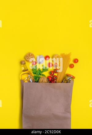 Olio d'oliva, pasta, tagliatelle, olive, uova, pomodori ciliegini, aglio in un sacchetto di carta su sfondo giallo Foto Stock