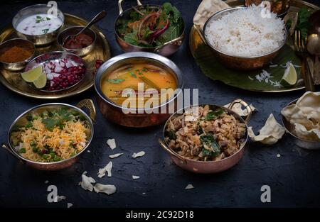 Piatti vegetariani dell'India del Sud serviti su piatti e vassoi tradizionali, sfondo nero Foto Stock