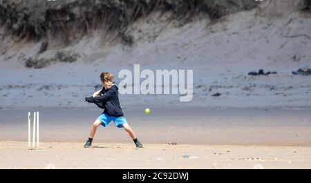 Anglesey, Galles del Nord, Regno Unito. Regno Unito Meteo: Martedì 28 luglio 2020, il clima caldo e il cielo blu a Newborough Beach, a ovest di Anglesey, mentre la gente si riverseranno sulla costa dopo un fine settimana di pioggia nel Galles del Nord. Un ragazzo in pieno swing che gioca a cricket a Newborough Beach sull'isola di Anglesey nel Galles del Nord © DGDImages/AlamyNews Foto Stock