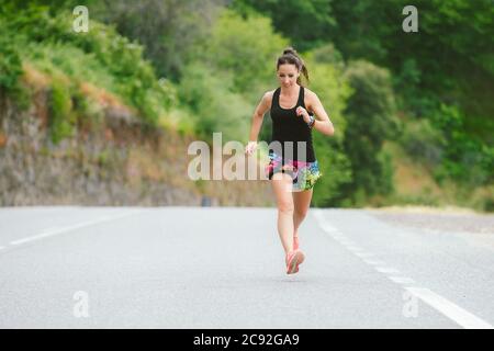 Donna con camicia nera e pantaloncini colorati per lo sport correre su strada Foto Stock