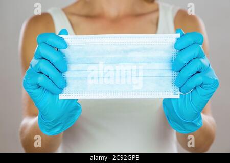 Donna con guanti di protezione blu che tengono la maschera chirurgica davanti a lei Foto Stock