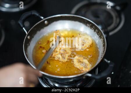 Primo piano delle pinze con le mani dello chef mentre cucinano fritti calamari in una padella Foto Stock