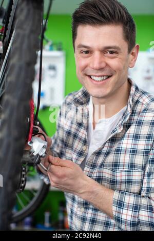 Ritratto di uomo piccolo proprietario di affari che ripara gli ingranaggi nel negozio di riparazione della bicicletta Foto Stock