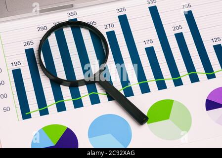 Lente di ingrandimento e diagrammi in vetro sul desktop. Concetto aziendale e analisi dei dati. Una vista dall'alto di un layout piatto. Foto Stock