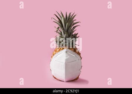 Ananas con maschera protettiva su sfondo rosa. Summer COVID-19 Concept Foto Stock