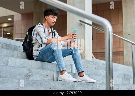 Young afro usa il suo cellulare mentre è seduto le scale Foto Stock