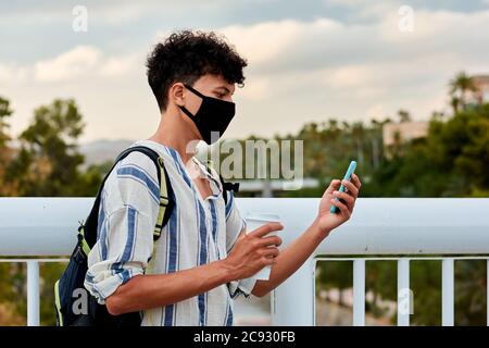 Il giovane uomo con capelli afro e maschera sta usando il suo cellulare la strada Foto Stock