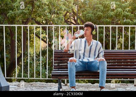 Ragazzo con i capelli afro beve caffè mentre è seduto su una panchina Foto Stock