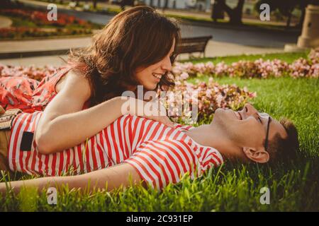 Storia d'amore, giovane ragazzo e ragazza che giace su erba verde, abbracciandosi l'un l'altro nel parco e trascorrendo il tempo insieme Foto Stock