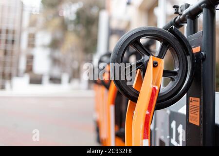 I veicoli ecologici. Scooter elettrico arancione in fila situato presso il banco di noleggio dei trasporti urbani. Closeup delle ruote. Foto Stock