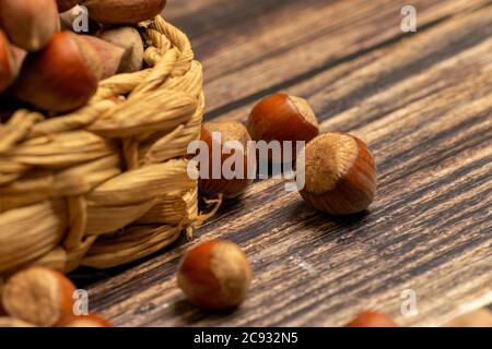 Nocciole in un cesto di vimini e nocciole sparse su uno sfondo di legno. Primo piano Foto Stock