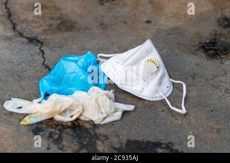 COVID-19 concetto di rifiuti o rifiuti. Guanti scartati, maschera medica e maschera N95 gettati via dopo l'uso sotto la pioggia all'aperto. Foto Stock