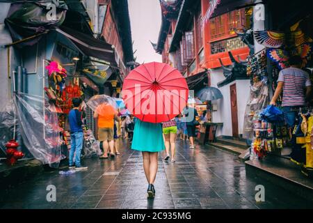 La donna della gente che cammina nella via dello shopping di chinatown. Giorno piovoso turista sotto ombrello orientale rosso in vicoli stretti sulla cina viaggio a Shanghai Foto Stock