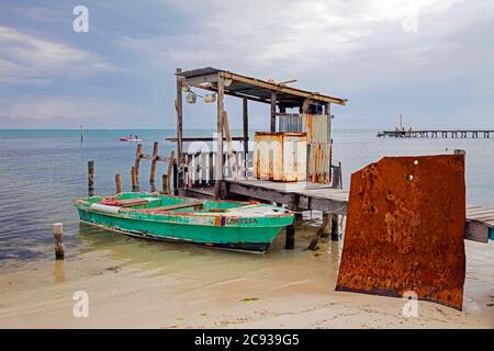 Piccola barca di pesca sulla spiaggia e vecchio molo di legno su Caye Caulker / Cayo Caulker, isola corallina al largo della costa del Belize nel Mar dei Caraibi Foto Stock