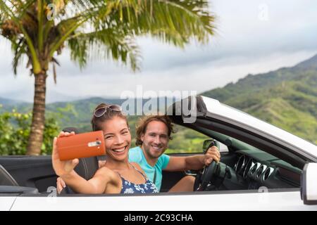 Selfie vacanze auto. Coppia che si diverte durante il viaggio estivo facendo foto con smartphone durante il viaggio. Giovani multirazziali che guidano Foto Stock