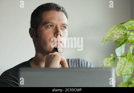 Bell'uomo pensieroso davanti al suo laptop in ufficio. Foto Stock