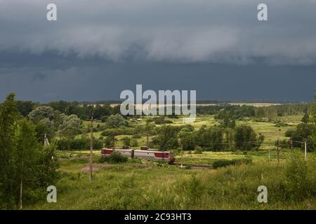 Vista dalla cima della collina sulla pianura con un temporale in avvicinamento e un treno in primo piano, la regione di Mosca, Russia Foto Stock