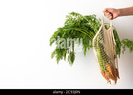 Mano maschile con carota in una griglia di cibo su uno sfondo bianco parete, un agricoltore tiene verdure appena raccolte con foglie verdi, raccolto fresco Foto Stock