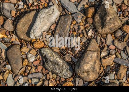 Guardando verso il basso su una parte asciutta del letto del fiume che ha diversi tipi di rocce colorate e pietre con piccoli ciottoli mescolati in sfondi closeup e te Foto Stock