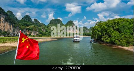 Yangshuo, Cina - Agosto 2019 : bandiera nazionale della Cina rossa che fluttering su un albero sul ponte della barca turistica turistica in un viaggio sul magnifico li Foto Stock