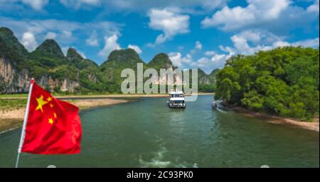 Yangshuo, Cina - Agosto 2019 : bandiera nazionale della Cina rossa che fluttering su un albero sul ponte della barca turistica turistica in un viaggio sul magnifico li Foto Stock