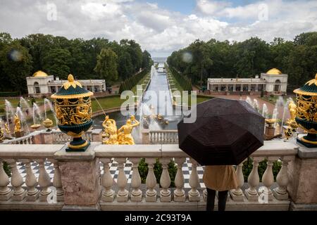 San Pietroburgo, Russia - 23 luglio 2020 UNA donna si erge sotto un ombrello e guarda la fontana della Grande cascata e le attrazioni del complesso del Palazzo reale a Peterhof, Russia, sotto la pioggia battente Foto Stock