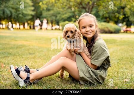 una ragazza è seduta su un prato verde con un cane di poodle Foto Stock