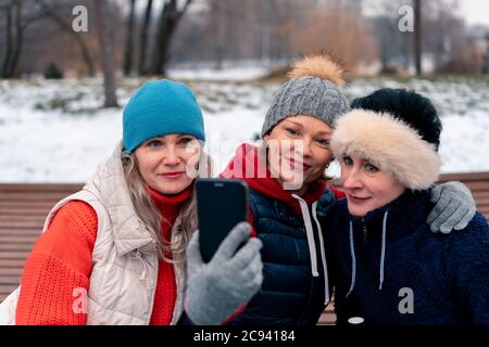 Donne mature sorridenti e facendo Selfie nel parco dopo l'allenamento attivo all'aperto. Amici di mezza età che trascorrono il tempo insieme Foto Stock