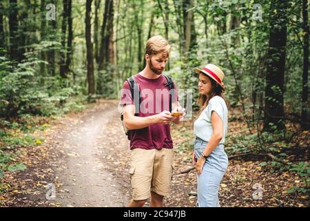 Escursionisti che utilizzano il gps mobile per le indicazioni. Felice coppia che controlla smartphone nel bosco durante il viaggio backpacking. Giovane coppia gioiosa che usa la mappa gps Foto Stock