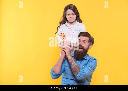 Dalo a me. Infelice bambino prendere caramella dalle mani dei padri. Negozio di caramelle. Lollipop o sucker sul bastone. Dolcetto. Fabbrica di caramelle e dolciumi. Torsione non si può resistere, copia spazio. Foto Stock