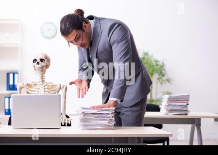 Giovane dipendente e scheletro in ufficio Foto Stock