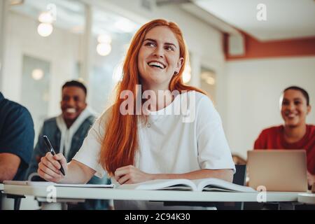 Donna che presta attenzione in lezione. Studentessa che ascolta l'insegnante e sorride seduto in classe. Foto Stock