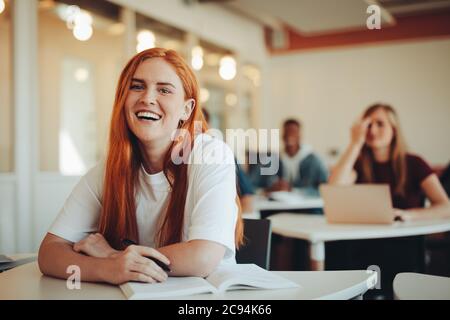 Ritratto di sorridente ragazza seduta in classe universitaria. Studentessa nella sala delle lezioni delle scuole superiori che guarda la macchina fotografica e sorride. Foto Stock