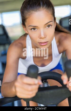 Donna asiatica allenamento cardio a casa in bicicletta indoor. Allenati per entrare in forma. Concetto di perdita di peso. Giovane ragazza motivata e focalizzata Foto Stock