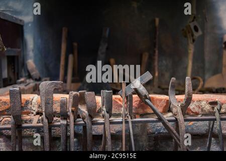 Vecchie pinze storiche e pinze di fabbro appese su fucina arrugginita di fronte al camino Foto Stock