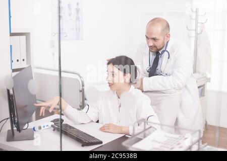Team di giovani medici che lavorano insieme sul computer nella stanza dell'ospedale. Medici che indossano cappotti e stetoscopio. Foto Stock