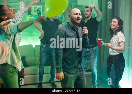 Allegro calvo uomo che fa karaoke per i suoi amici alla festa. Foto Stock