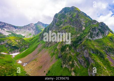 La cima di una montagna rocciosa su un crinale con prati verdi e neve, ruscelli. Vista aerea del drone Foto Stock